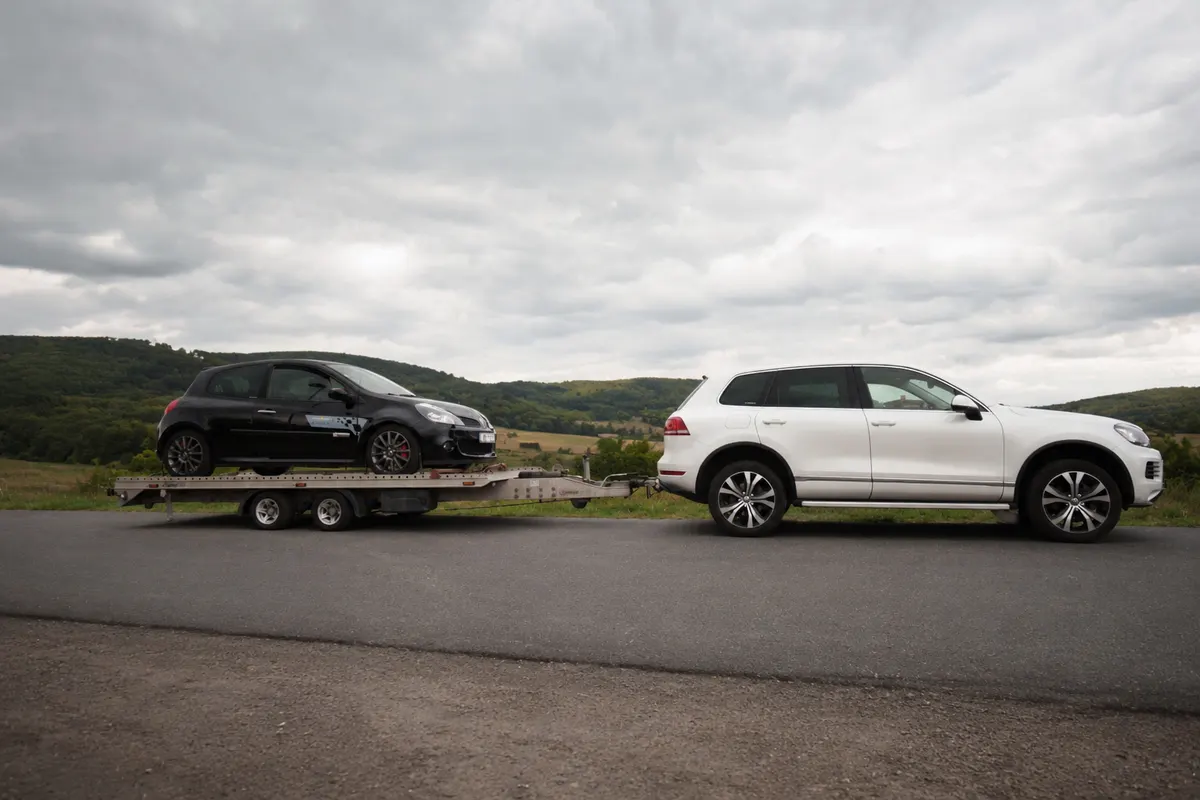 Bílý Volkswagen Touareg s přívěsem přepravující černý vůz
